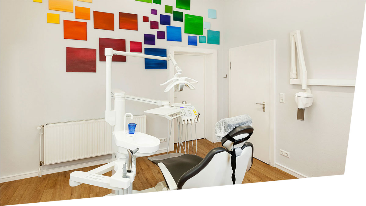 Moderner weißer Behandlungsraum mit bunter Wandgestaltung in der Praxis Dr. Behr & Dr. Trojanski